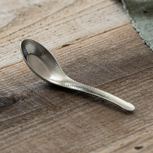 Nagomi Hammered Style stainless steel ramen spoon with tsuchime texture and deep rounded bowl, shown on a weathered wooden surface