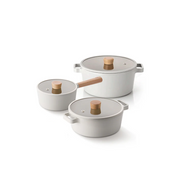 The Neoflam Fika 6-piece cookware set, showing the saucepan, pot, and stockpot in a light cream colour with wooden handles and matching glass lids.