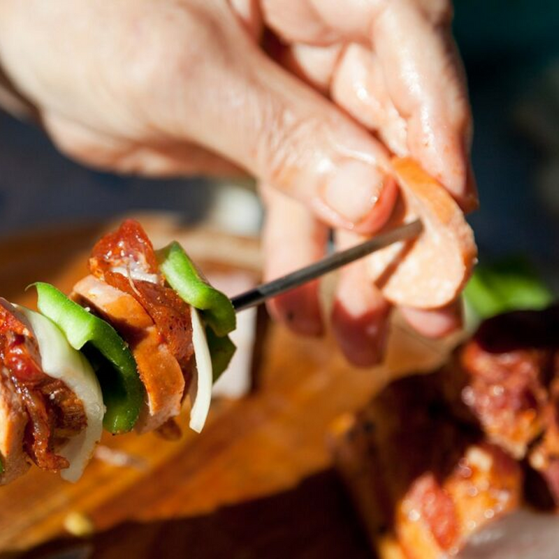 A hand carefully threads pieces of meat and fresh vegetables onto a Nippan Extra-Long Barbecue Skewer in preparation for grilling.