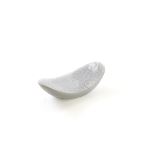 A white oval ceramic chopstick rest with a delicate swirl pattern embossed on its curved surface, isolated on a white background.