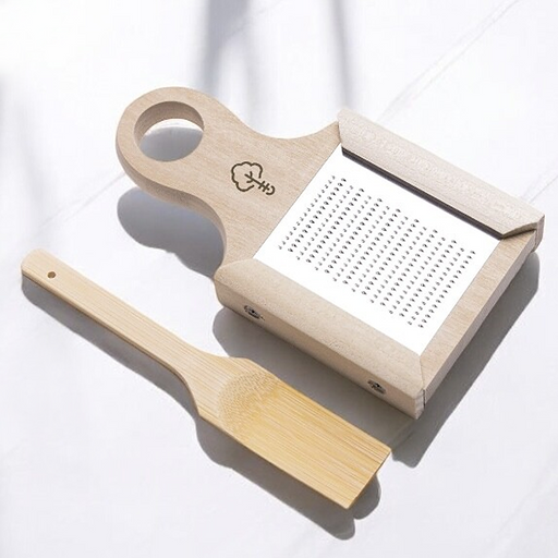 A Japanese wooden condiment grater with a stainless steel surface, displayed with a small bamboo scraper brush for gathering grated ginger or wasabi.