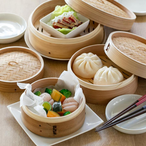 Pearl Life Bamboo Steamers in various sizes filled with dumplings and vegetables, displayed on a wooden table.