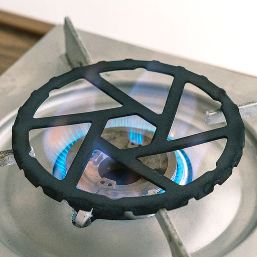 A black cast iron mini trivet placed on a gas stove burner, providing a stable platform for small cookware over the open flame.