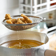 Pearl Life stainless steel deep frying strainer lifting freshly fried karaage from hot oil, with oil draining through the fine mesh basket over a stainless steel tempura pot.
