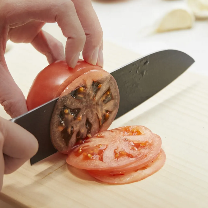 A close-up of a Remy Kuro Japanese Santoku knife slicing through a tomato, demonstrating the knife’s sharpness and the precision of its cut, with tomato juice highlighting the blade’s edge.