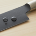 Close-up of the Remy Kuro Japanese Santoku knife’s blade with water droplets beading on the matte black surface, highlighting its hydrophobic properties.