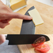 Demonstrative use of the Remy Kuro Japanese Santoku knife cutting through a block of butter, emphasizing the knife's sharp edge and non-stick black surface.