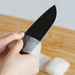 A hand carefully wiping the blade of a Remy Kuro Japanese Santoku knife with a soft cloth, emphasizing the knife’s smooth, black surface and crafted edge.