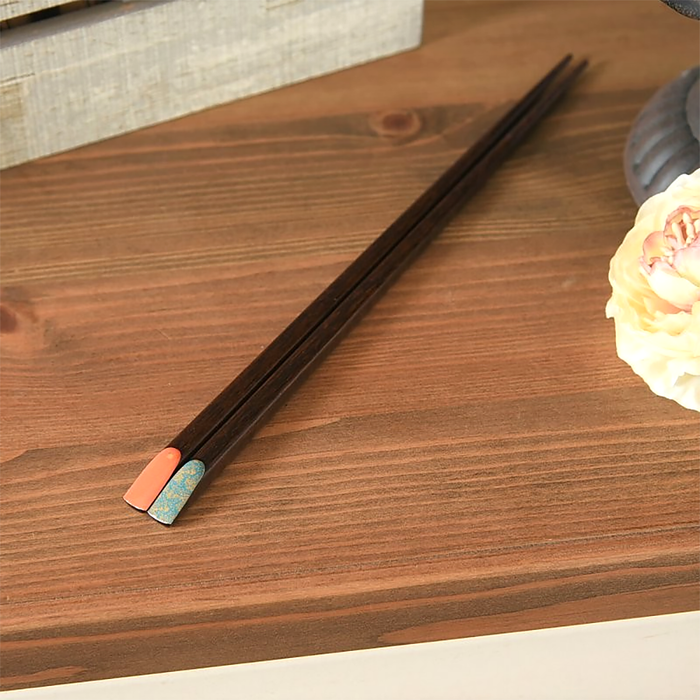 A pair of retro-style chopsticks with a rich wooden base. One tip features a coral finish adorned with subtle gold markings at the lower margin, while the other showcases a turquoise design with gold-flecked, leaf-like patterns.