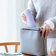 Person placing a Zojirushi Silm Vacuum Insulated Flask - 250ml (SM-MS25-VM) - Purple into a gray bag on a table.