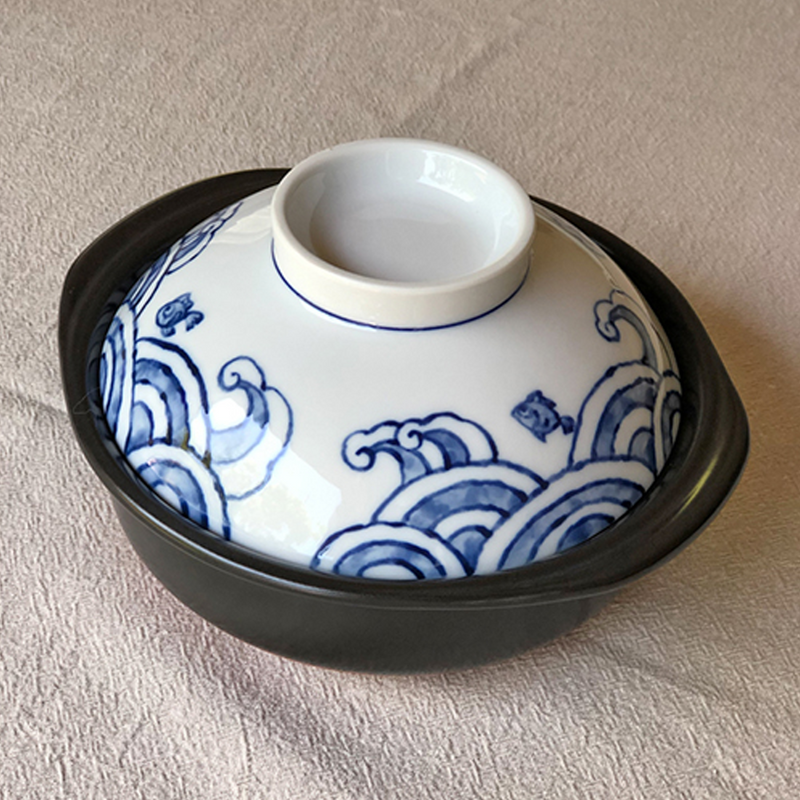 A product image of the Saji Tairyoumaru mini donabe, showing its dark clay base and the lid's traditional blue Japanese wave pattern.