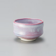 The Sakura Unofu matcha bowl (chawan), featuring a speckled pink and light blue glaze and an irregular rim, shown against a light grey background.

