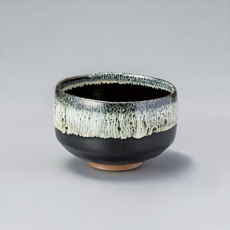 A Japanese Satsuma Tenmoku matcha bowl with a textured white glaze dripping over a matte black base, shown against a plain grey background.

