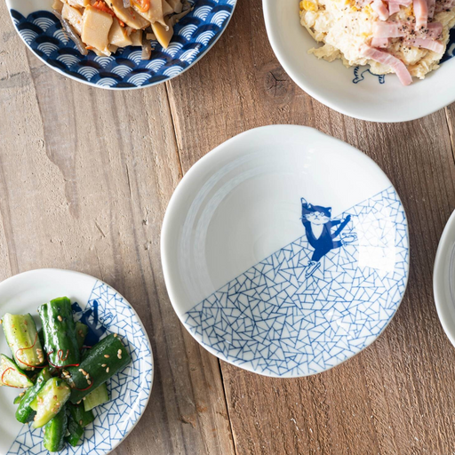 A white and blue Shichita Mino Yaki bowl with a cat and fractured-ice pattern, displayed on a wooden table with various side dishes.