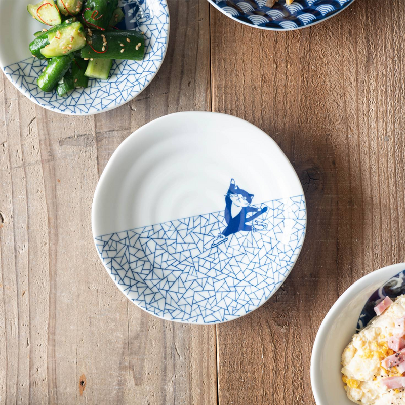 Top-down view of the Shichita Mino Yaki Cat Hyouretsumon Pattern Plate placed on a wooden surface, featuring a cat in blue ice skating across a geometric triangle pattern.


