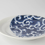 Close-up of the indigo Karakusa swirl pattern on the ceramic plate, showing the glossy finish and the playful cat detail at the edge.







