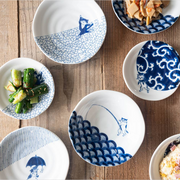 Cat fishing plate displayed among other blue-and-white cat-themed dishes on rustic wooden table.

