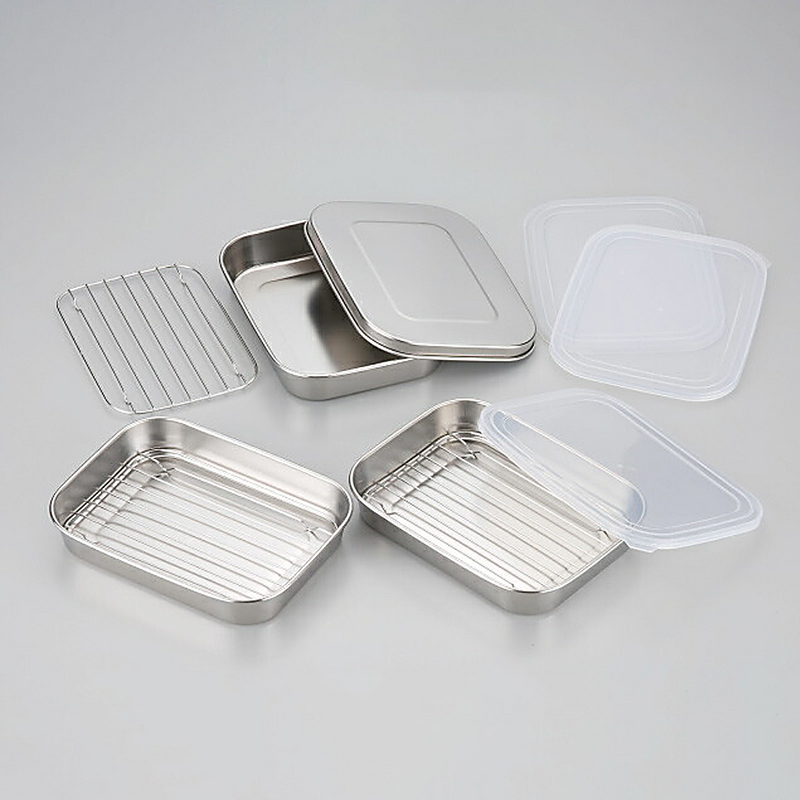 Various components of the Shimomura food prep set, including stainless steel trays, a wire rack, and lids, displayed on a grey surface.

