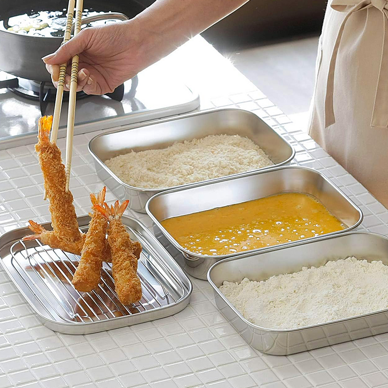 The Shimomura stainless steel food prep set being used to bread and drain fried tempura shrimp on a kitchen counter.

