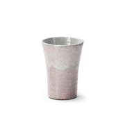 A Japanese Shino ware shochu cup, showing its tall, irregular shape and rustic, mottled pink and white glaze on a white background.
