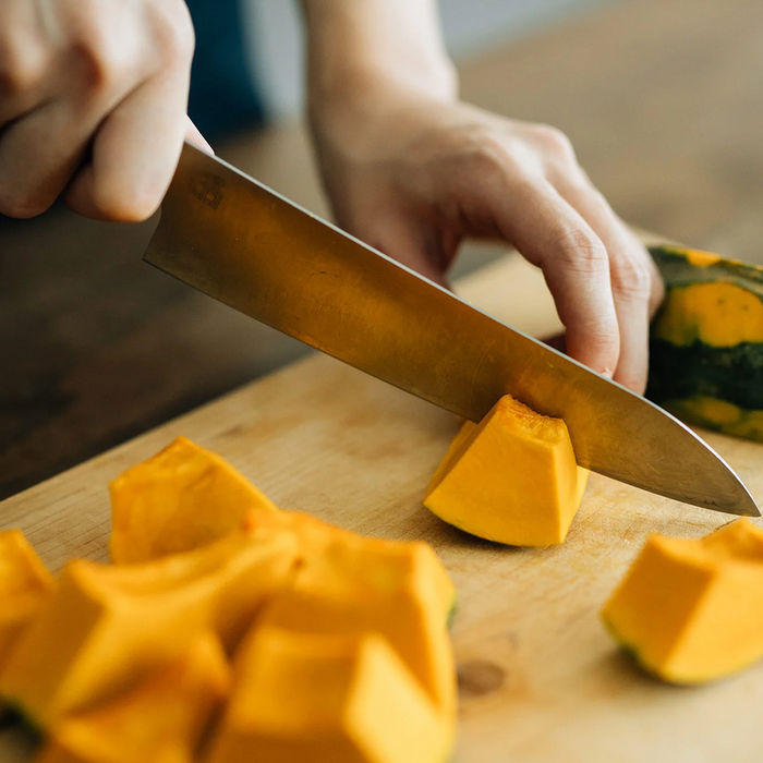 The Shizu Takumi Yuri Japanese Santoku Knife being used to chop a pumpkin into pieces, demonstrating its versatility and strength in handling different types of produce.