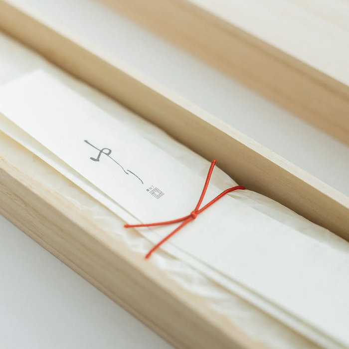 A close-up of the paper insert inside the wooden box, highlighting the intricate details of the packaging with a focus on the red string and the Japanese characters on the insert.