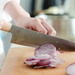 A person using the Shizu Takumi Yuri Japanese Santoku Knife to thinly slice a red onion on a wooden cutting board, showcasing the knife's precision and sharpness.