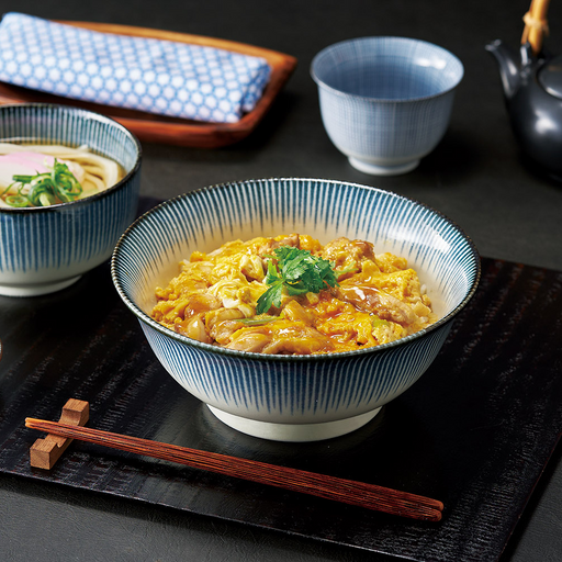 A lifestyle image of the Showa Seito donburi bowl filled with oyakodon (chicken and egg rice bowl), served on a traditional Japanese tray with chopsticks.

