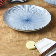 A Showa Seito Sendan Tokusa plate with its blue and white radial pattern, shown on a wooden table alongside chopsticks and chopstick rests.