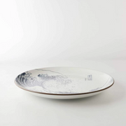 A low-angle side view of 'The Great Wave' 25cm dinner plate, highlighting its gentle curve and dark brown rim against a white background.

