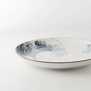 A low-angle side view of 'The Great Wave' dinner plate, highlighting its gentle curve and dark brown rim against a white background.


