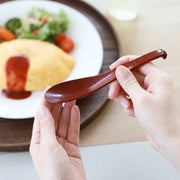 Hand holding the red Sunlife Japanese soup spoon over a plate of omurice