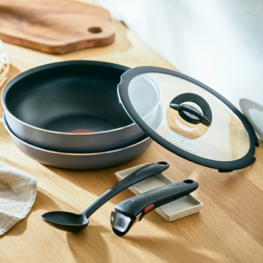 The T-fal Ingenio Neo 5-piece cookware set, including the stacked frying pan and wok, glass lid, cooking spoon, and detachable handle, arranged on a kitchen counter.