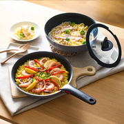 A T-fal Ingenio frying pan with handle attached serving paella, next to a saucepan of pasta on a dining table.