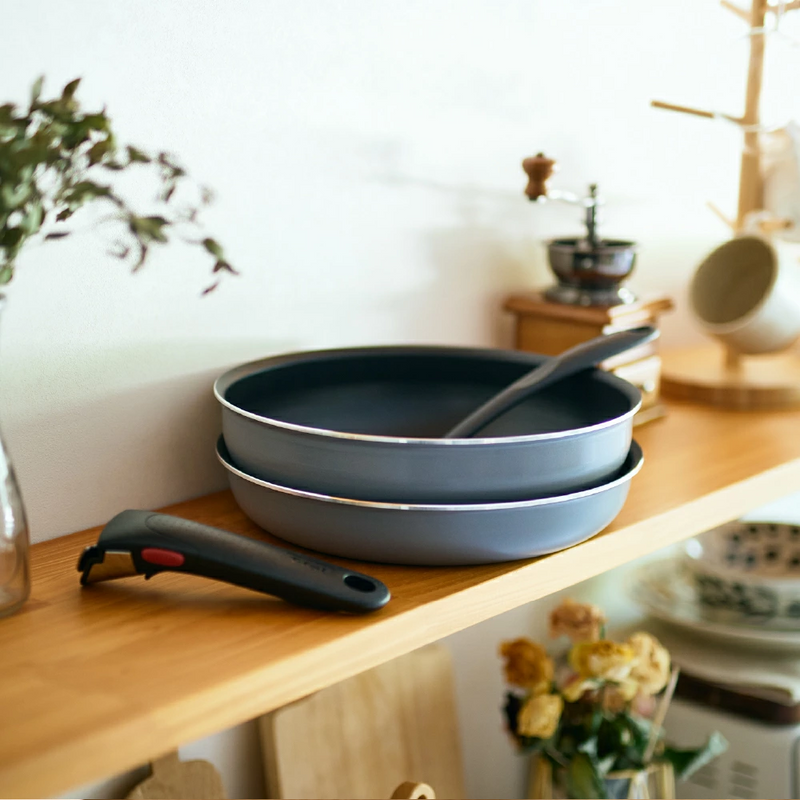 Two T-fal Ingenio Neo frying pans stacked for compact storage on a kitchen shelf, with the detachable handle placed next to them.

