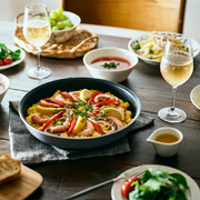 A T-fal Ingenio frying pan filled with paella served directly on a dining table alongside wine and side dishes.

