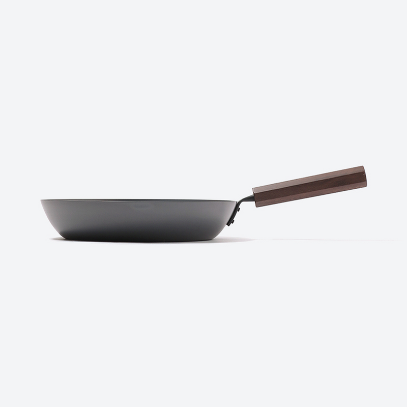 This image shows the sleek, minimalist side profile of the frypan, highlighting its sturdy carbon steel body and ergonomic wooden handle.