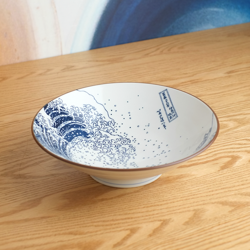 A lifestyle photo of 'The Great Wave' Japanese ramen bowl sitting on a wooden table, showcasing the iconic Hokusai artwork on its interior.

