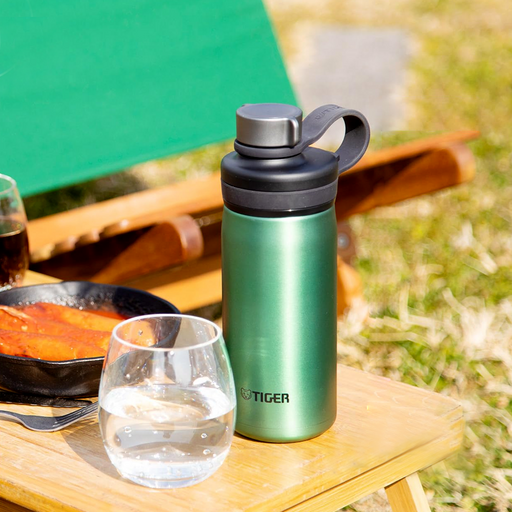A Tiger MTA-T050 vacuum insulated carbonated bottle in metallic emerald green with a black screw-top lid and integrated loop handle, sitting on a wooden outdoor table.