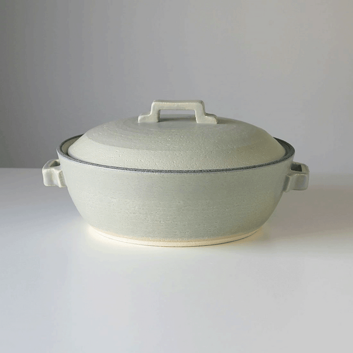 Close-up side view of the Tojiki Tonya Tstyle Donabe Japanese clay pot, showcasing its detailed silver-grey texture, the pot's side handles, and the signature lid handle.