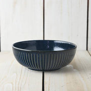 Side view of the Toki Takane Indigo Tokusa Bowl (20cm) on a white timber surface, showing the vertical stripe pattern