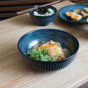 Toki Takane Indigo Tokusa Bowl (20cm) filled with a noodle salad on a wooden table, with a matching rice bowl and plate behind