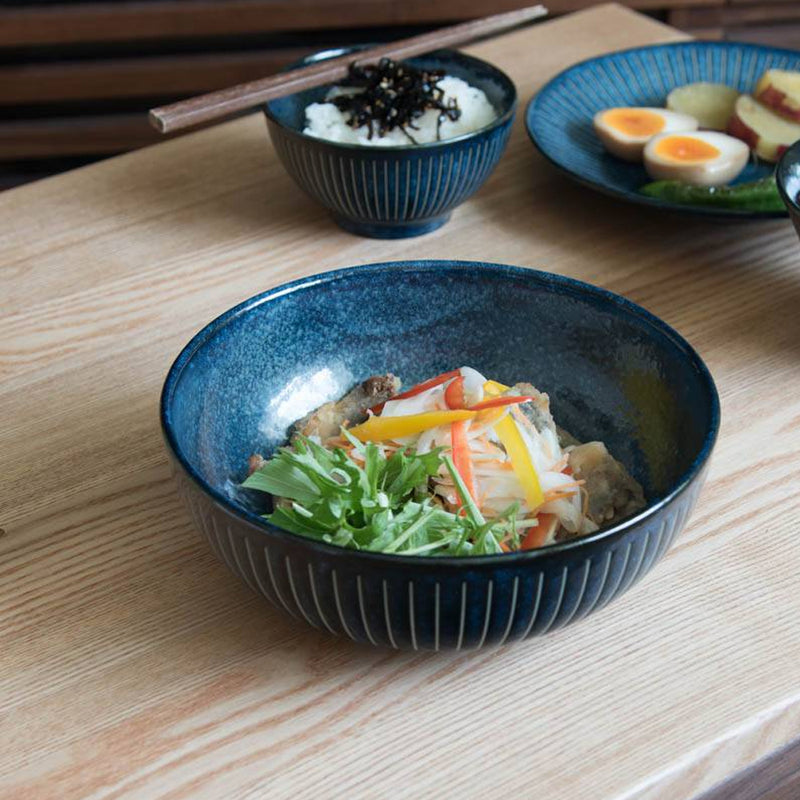Toki Takane Indigo Tokusa Bowl (20cm) filled with a noodle salad on a wooden table, with a matching rice bowl and plate behind