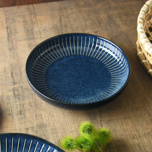 A deep blue Japanese pasta plate (20cm) featuring a radial white 'Tokusa' pinstripe pattern, sitting on a wooden table.