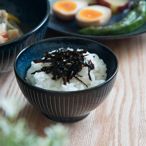 A dark blue Japanese rice bowl featuring a vertical 'Tokusa' pinstripe pattern, filled with white rice and topped with sesame-garnished kelp.