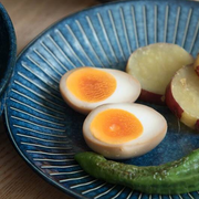 A close-up of a soft-boiled egg and sweet potato served on the Tokusa Indigo Dinner Plate (20cm), showing the food's texture against the plate's striped pattern.