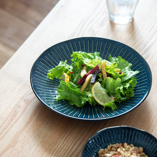 A fresh green salad served on the Tokusa Indigo Dinner Plate (23cm), which is sitting on a light wood dining table.
