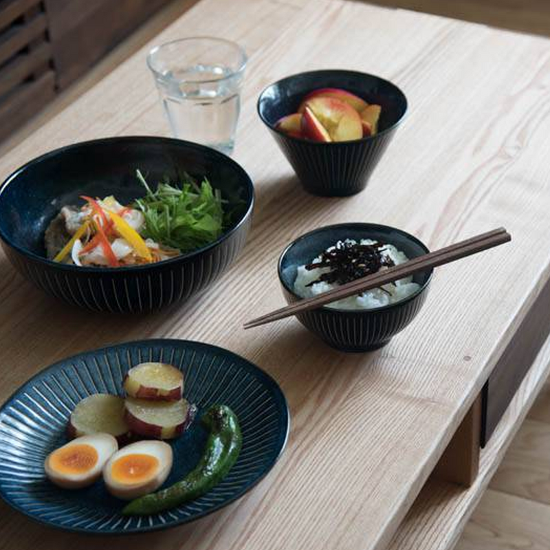 A meal served on a wooden table using the Tokusa Indigo collection, with the 13cm bowl holding rice and another holding fruit.

