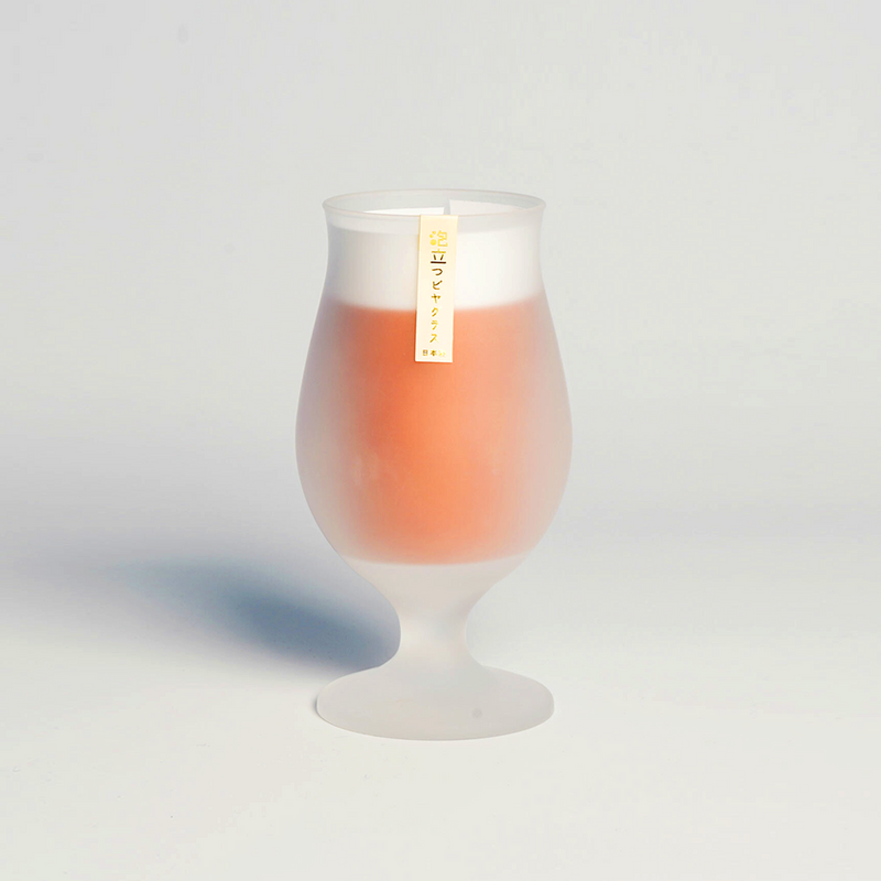 Frosted tulip beer glass filled with amber beer and foam, photographed against a plain white background with a Japanese label attached.
