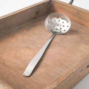 A Japanese-style stainless steel slotted ladle with a textured hammered finish, resting on a rustic wooden tray.